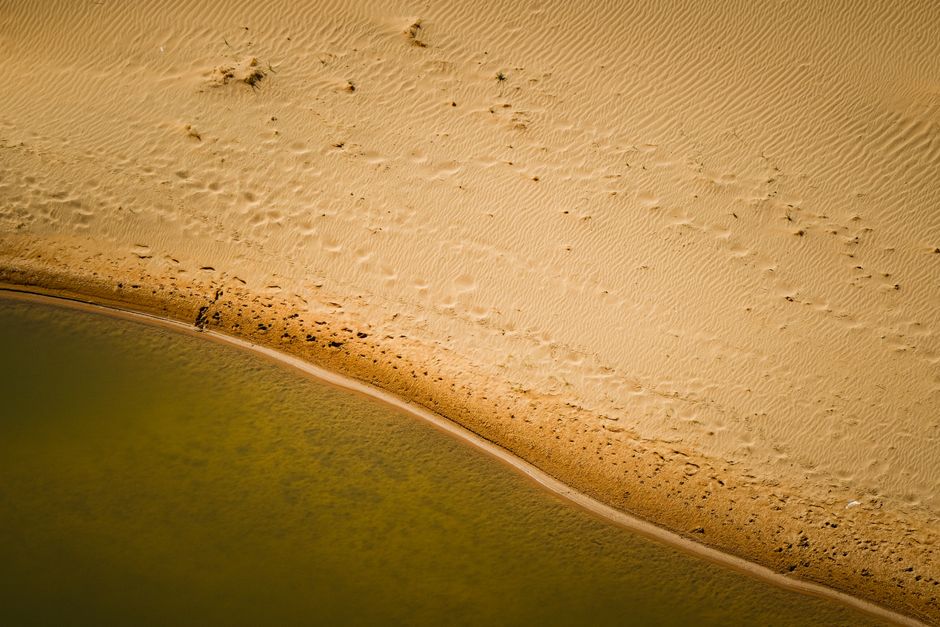 Serene aerial capture of a sandy beach meeting a calm sea, showcasing nature's peaceful landscape.