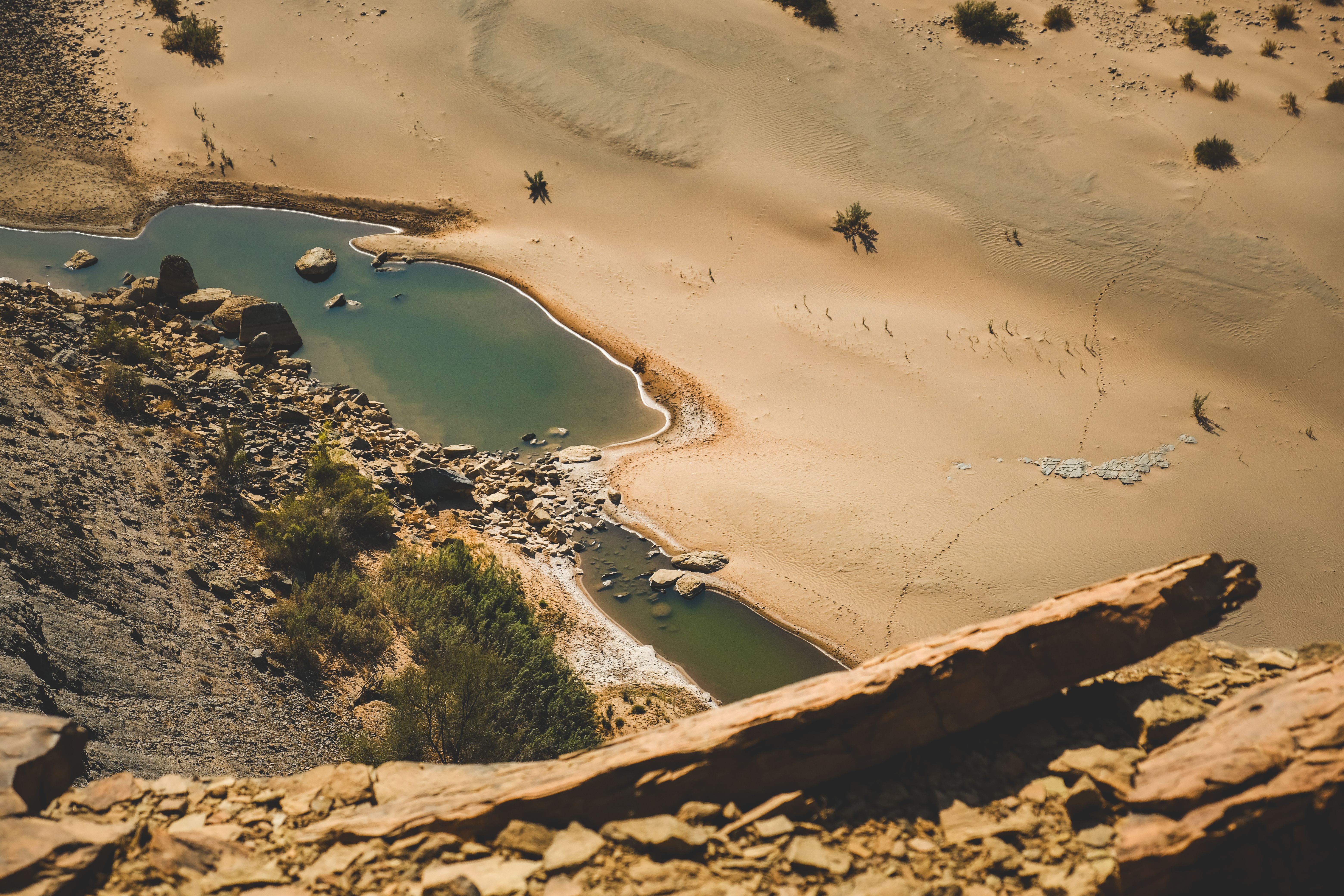 Natural green rock pools beside sand and boulders seen from a rocky ledge