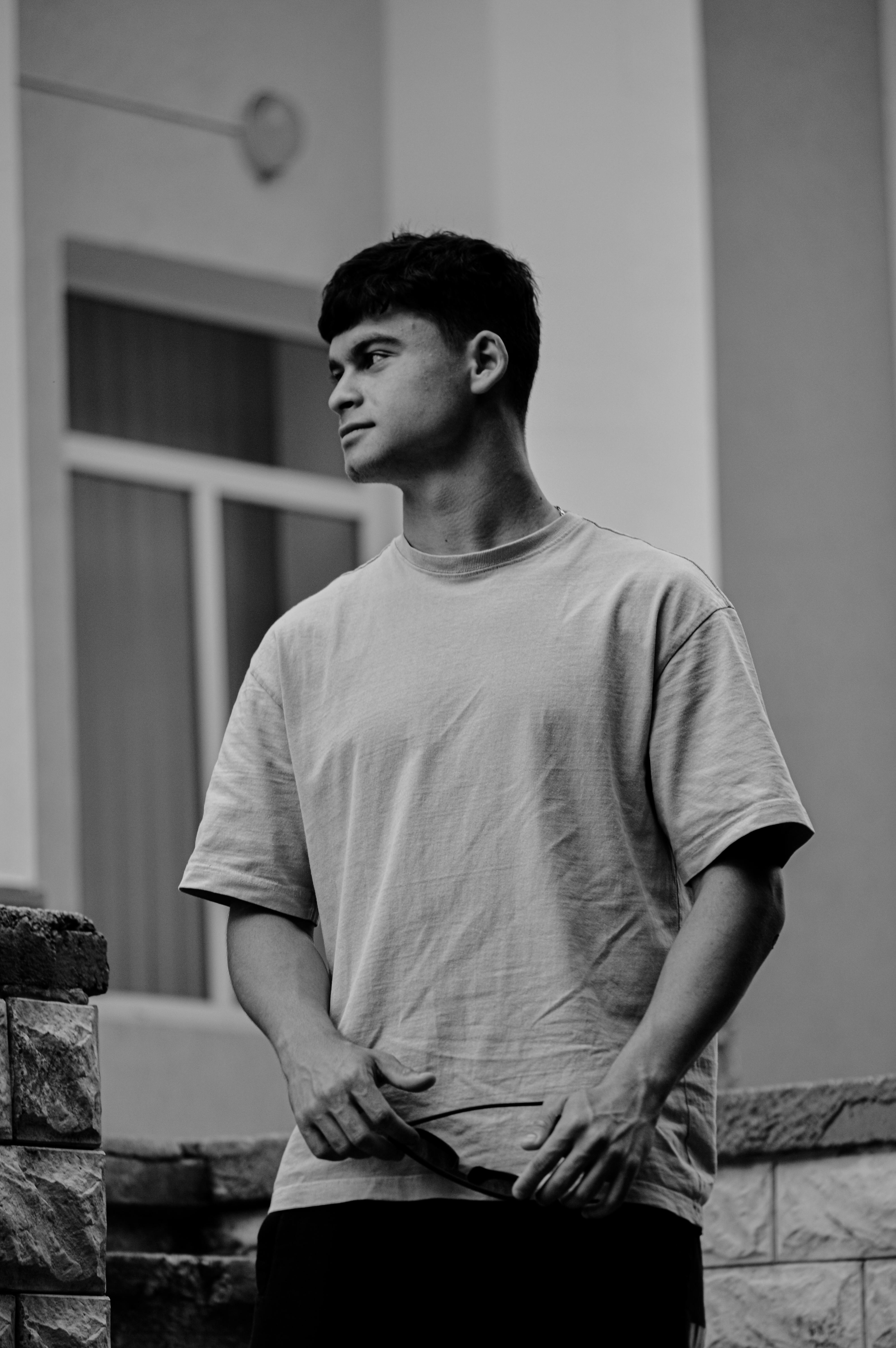 A black and white portrait of a young man in a casual t-shirt, looking thoughtful outdoors.