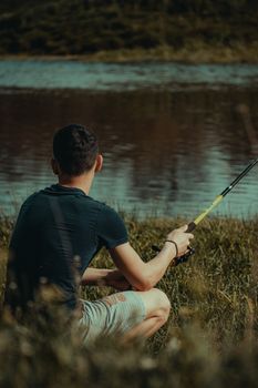 A man in a t-shirt and shorts enjoys fishing by a serene countryside river.