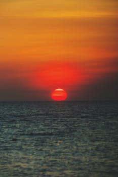 Sunset over a tranquil ocean, showcasing vibrant orange and red hues in the sky.