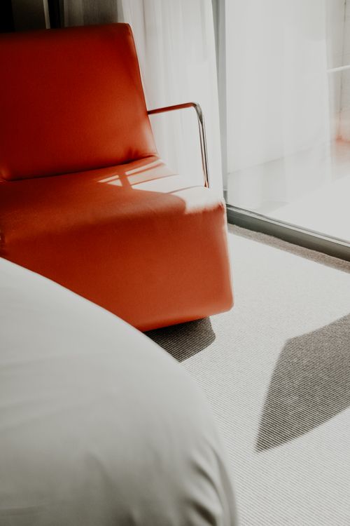Free A modern red sofa bathed in sunlight by a window, showcasing minimalist design. Stock Photo