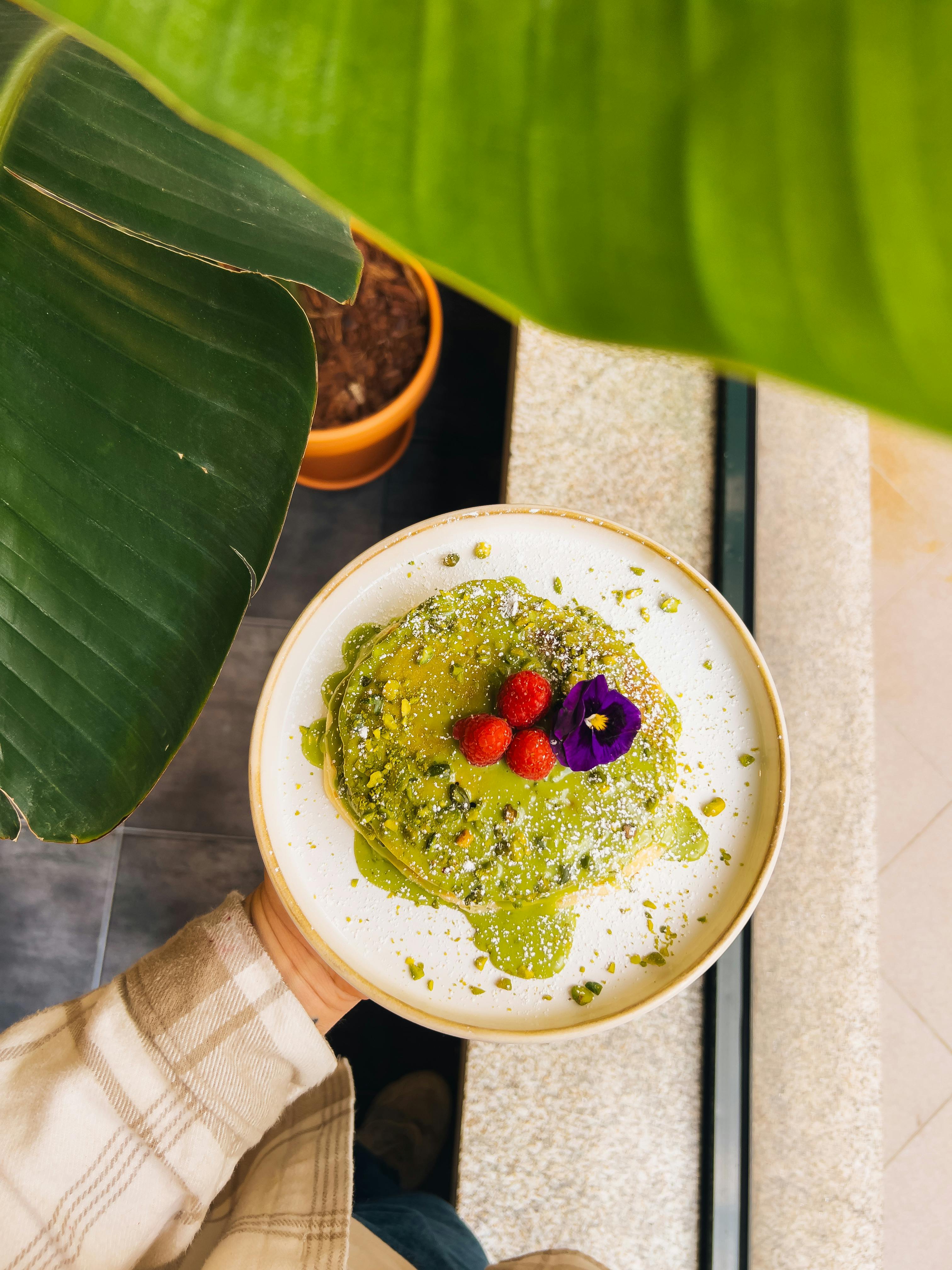 Colorful matcha pancakes topped with berries and an edible flower, held by a person.