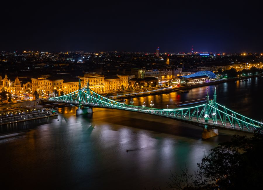Freedom Bridge in Budapest beautifully lit across the Danube River at night, showcasing the city skyline.