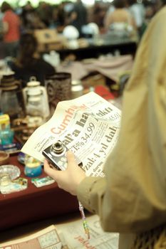 A person browsing a flea market, holding a vintage newspaper with retro items around.
