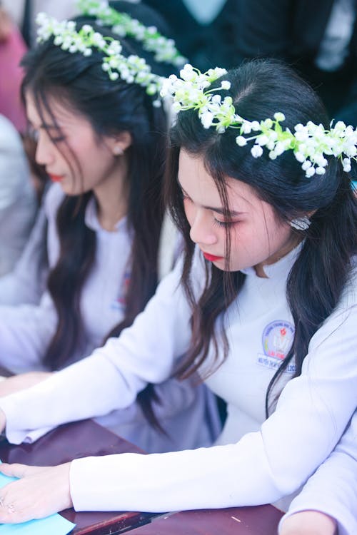 Two young women in white flower crowns are writing on paper