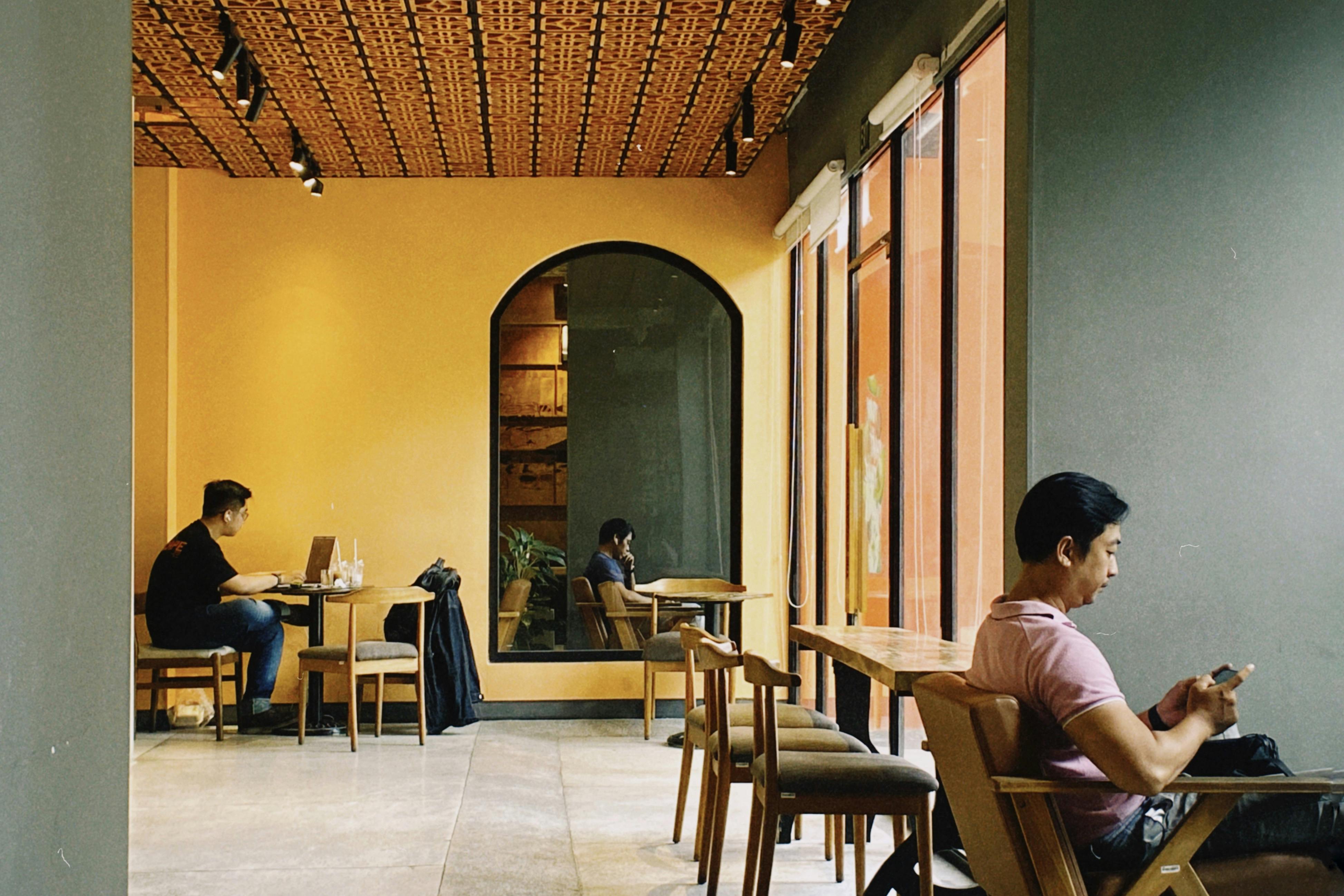 Freelancers working on laptops inside a modern coworking café with natural light, shared tables, and a relaxed professional atmosphere.