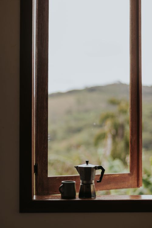 Free A serene still life of a moka pot and coffee cup on a windowsill with an outdoor view. Stock Photo