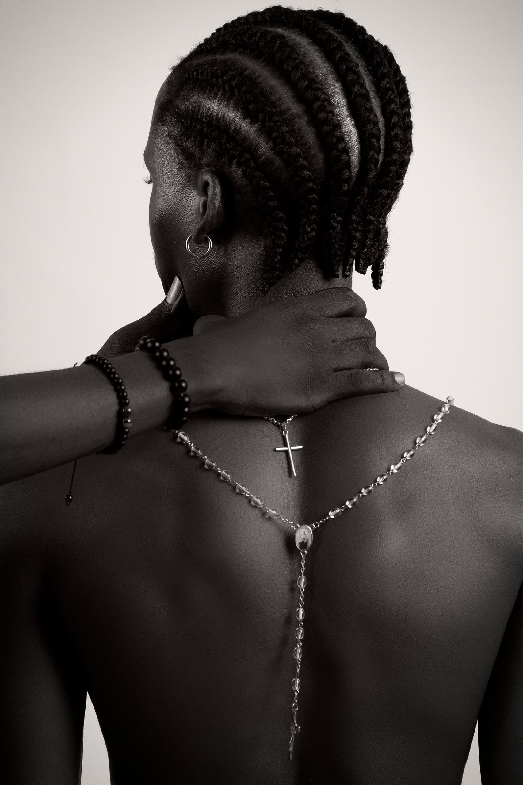 Striking black and white photo of a woman with braided hair and rosary cross pendant.