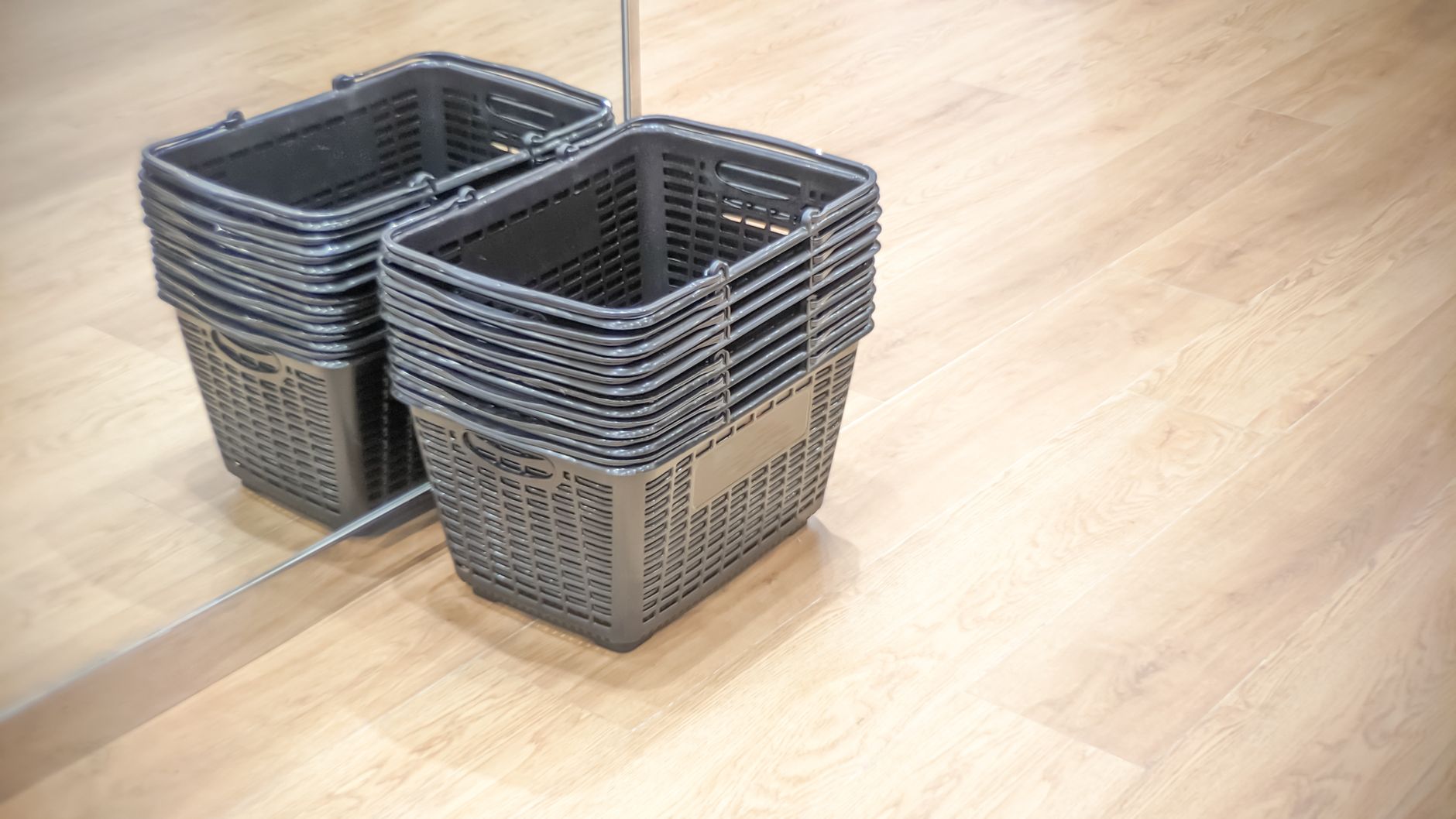 A stack of empty shopping baskets reflected in a mirror on a wooden floor.
