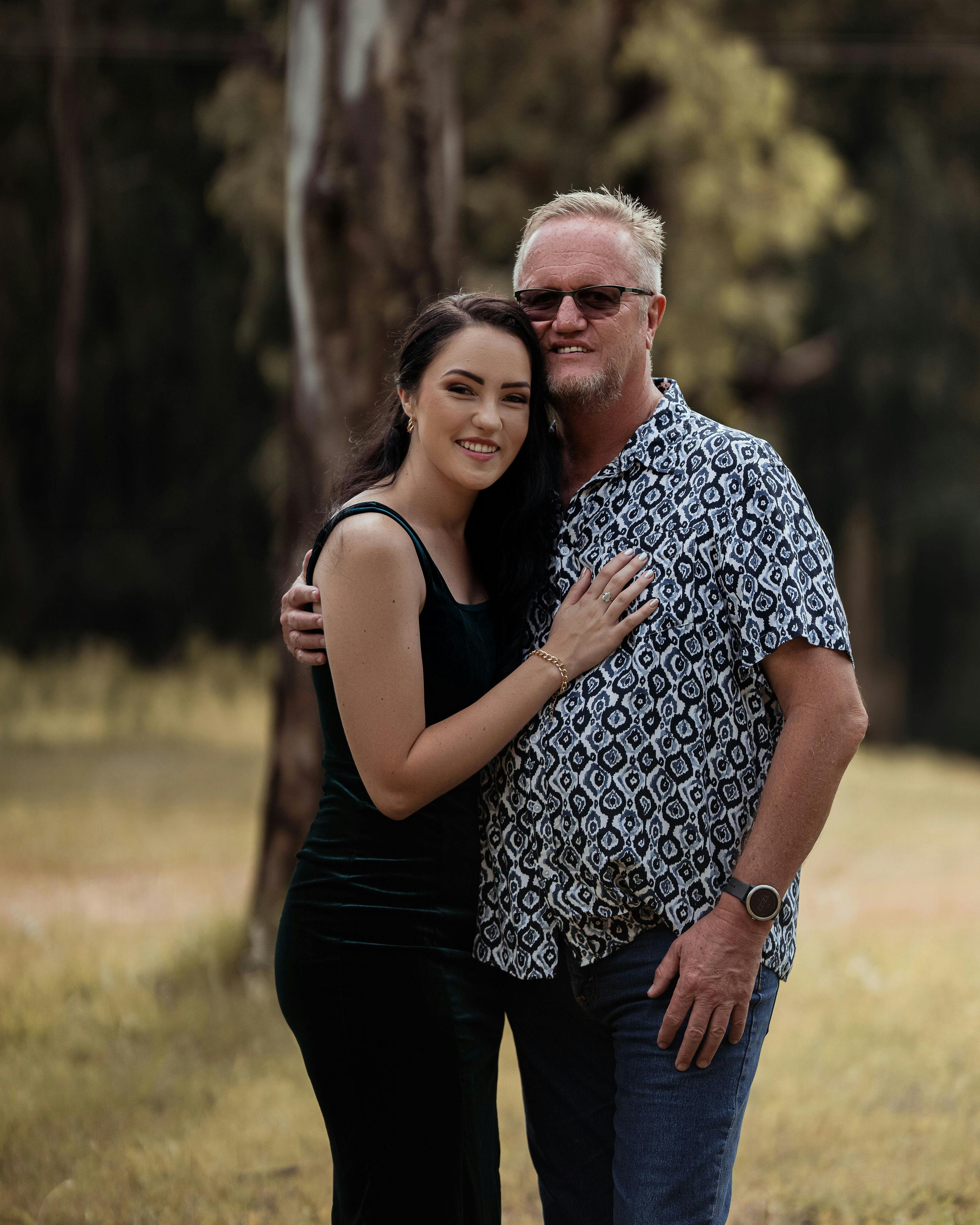 A father and daughter embrace in a scenic outdoor park, enjoying their togetherness.