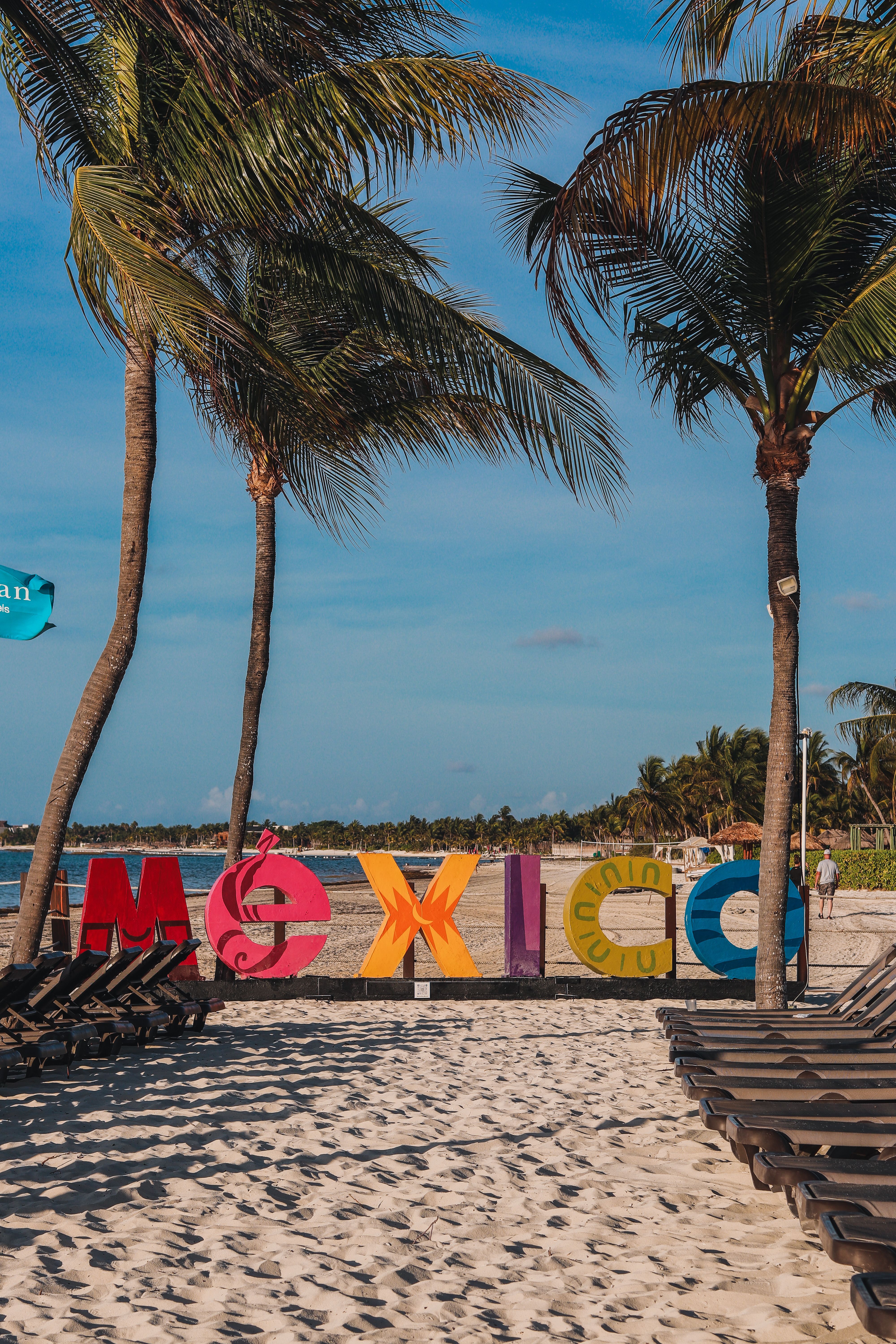 Colorful Mexico sign on a sandy beach with palm trees, perfect for travel enthusiasts.