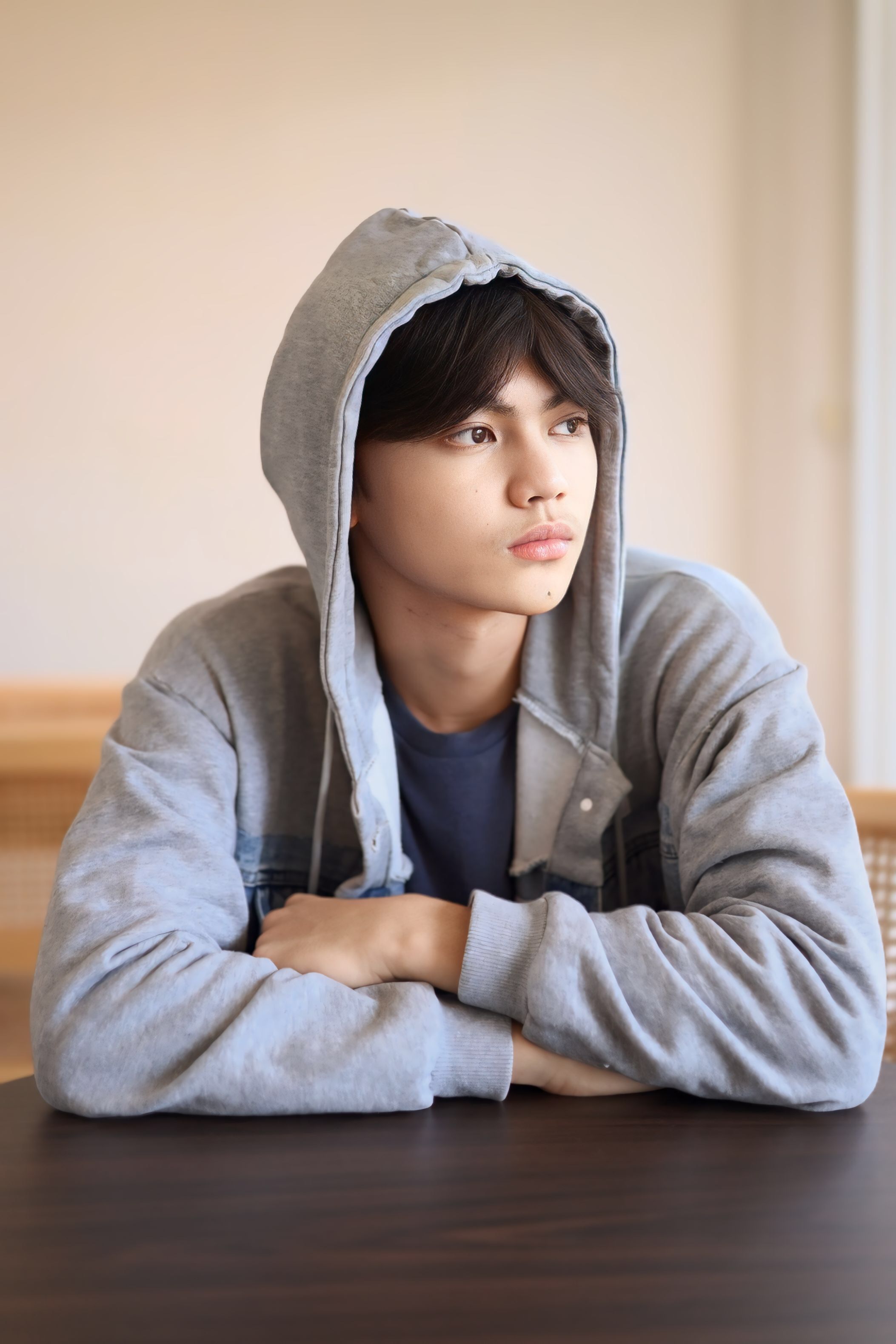 Portrait of a young man in a grey hoodie sitting at a table, gazing thoughtfully.