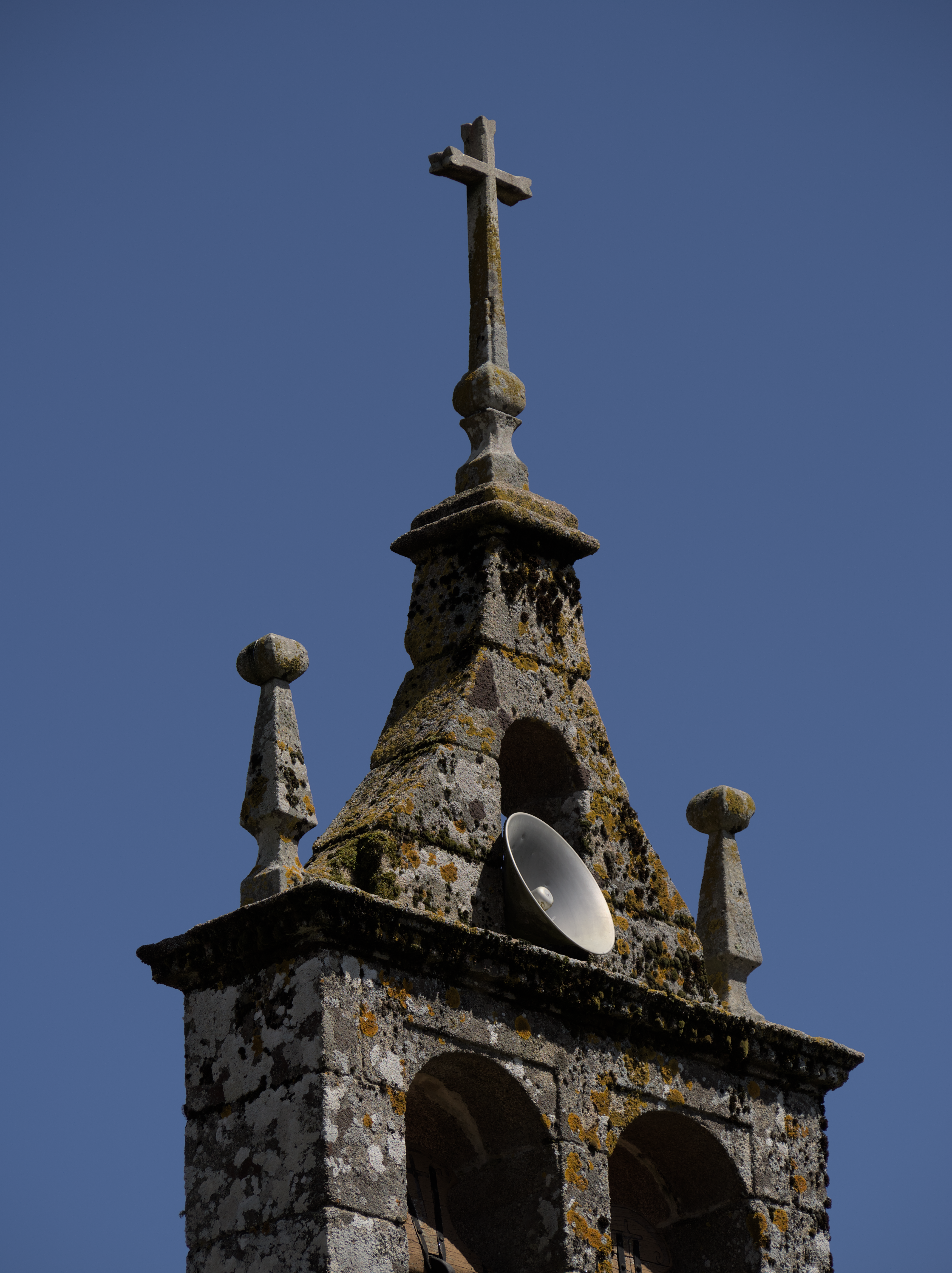 Stone church rooftop with a cross against a clear blue sky, showcasing architectural details.