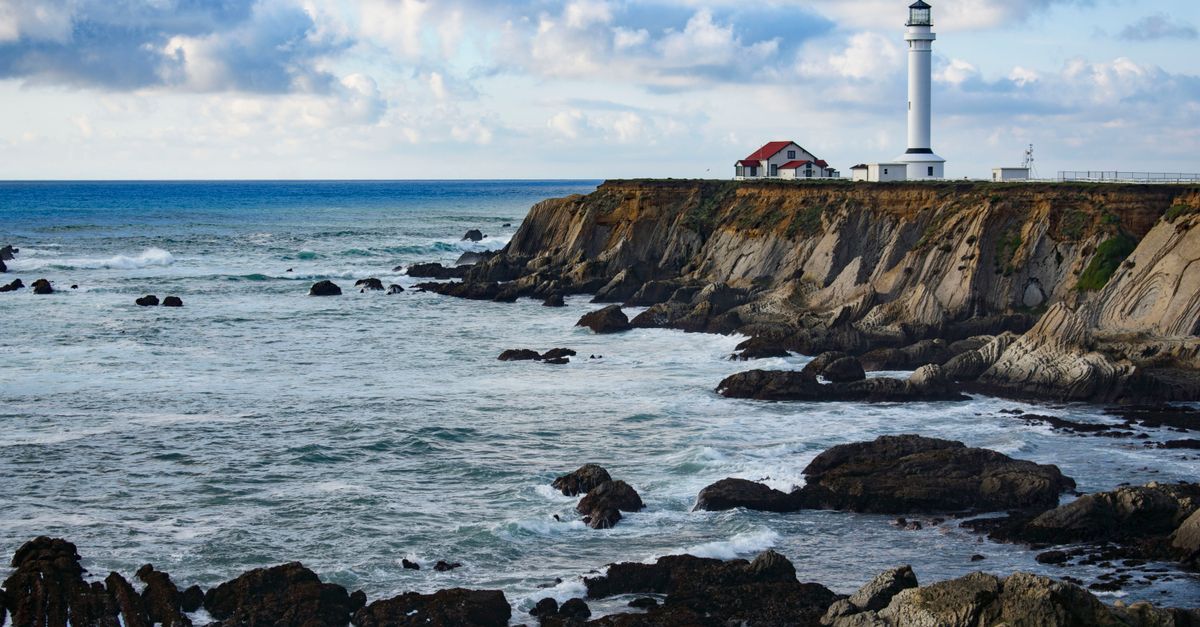 Scenic view of Point Arena Lighthouse on the rocky California coast with waves crashing against the cliffs.