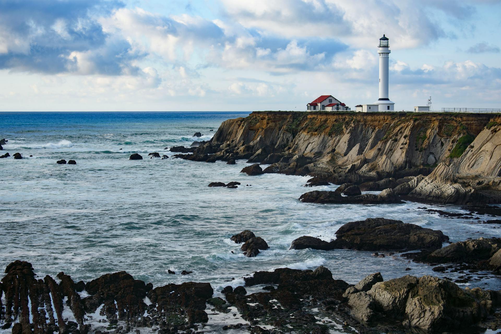 Scenic view of Point Arena Lighthouse on the rocky California coast with waves crashing against the cliffs.