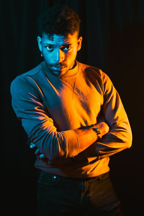 Free A moody portrait of a young man in colorful studio lighting with arms crossed. Stock Photo