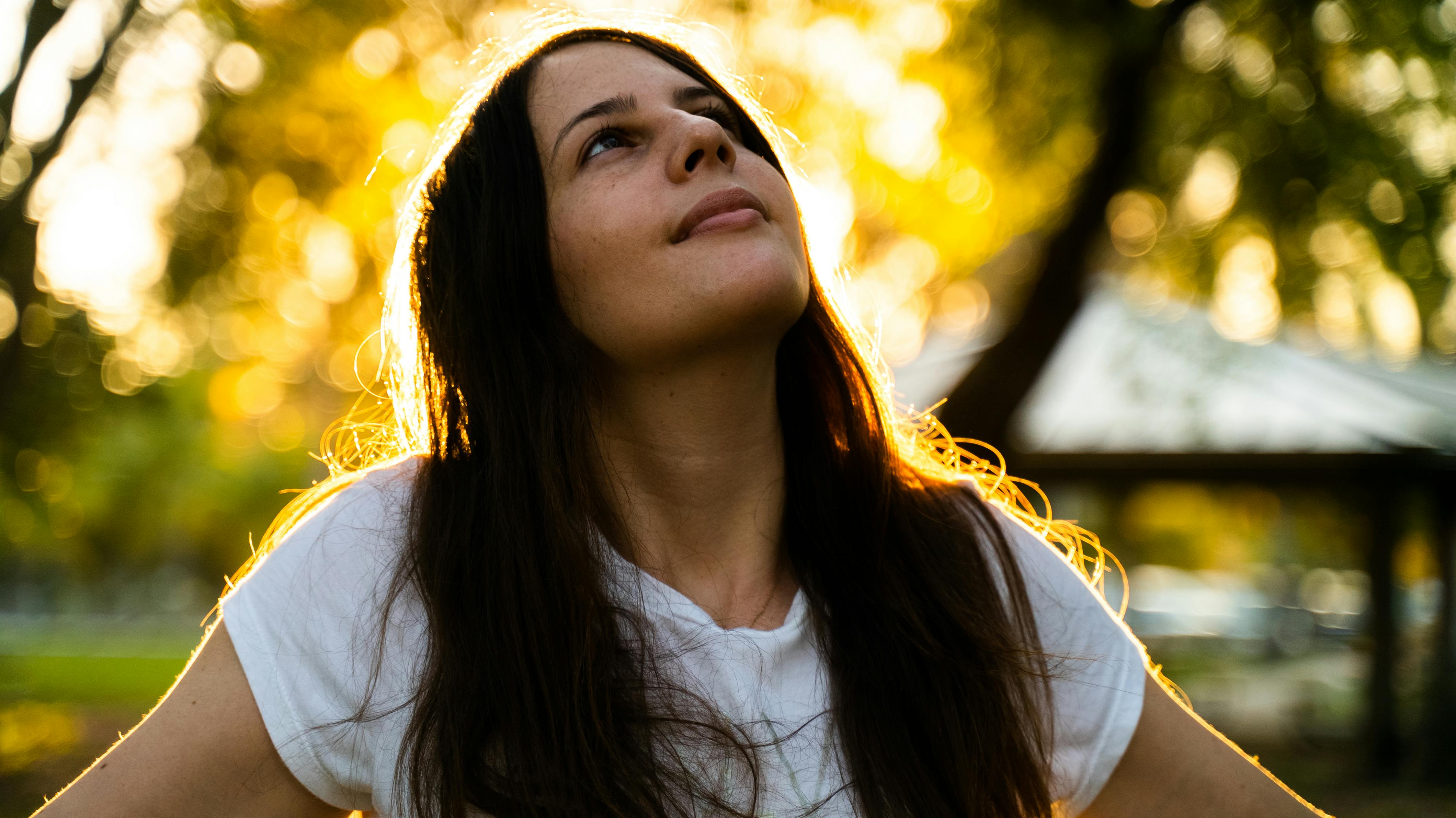 阳光明媚的公园里，一名身穿白衬衫的女子若有所思地抬起头