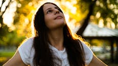 阳光明媚的公园里，一名身穿白衬衫的女子若有所思地抬起头