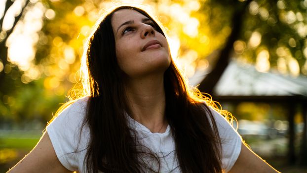 阳光明媚的公园里，一名身穿白衬衫的女子若有所思地抬起头