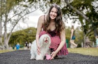 一位开朗的女子穿着红色连衣裙，和她毛茸茸的狗在风景优美的公园里合影