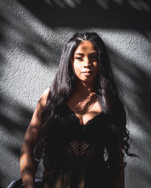 Photo of Woman in Black Lace Top Posing In Front of Gray Wall