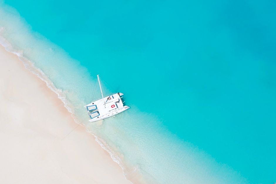 Drone shot of a white boat on a pristine beach with clear turquoise waters.