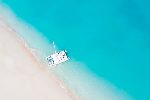 Free Drone shot of a white boat on a pristine beach with clear turquoise waters. Stock Photo