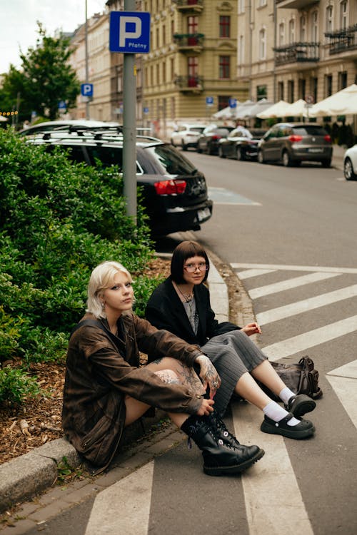 Two women sitting on the curb in front of a building