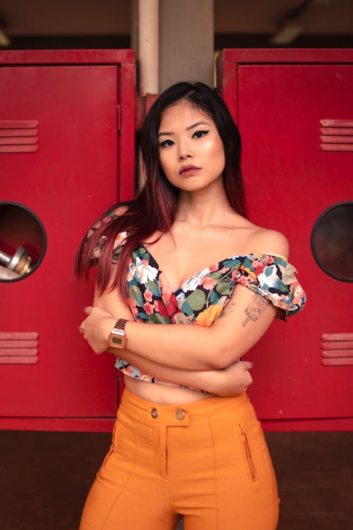 Photo of Woman in Floral Off-shoulder Crop Top and Orange Fitted Pants Posing with Her Arms Crossed