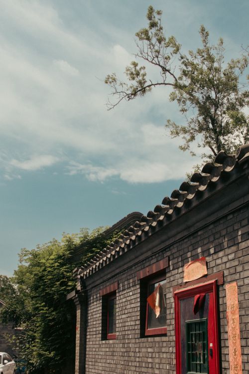 Free Charming traditional brick house with red details and lush greenery under a clear blue sky. Stock Photo