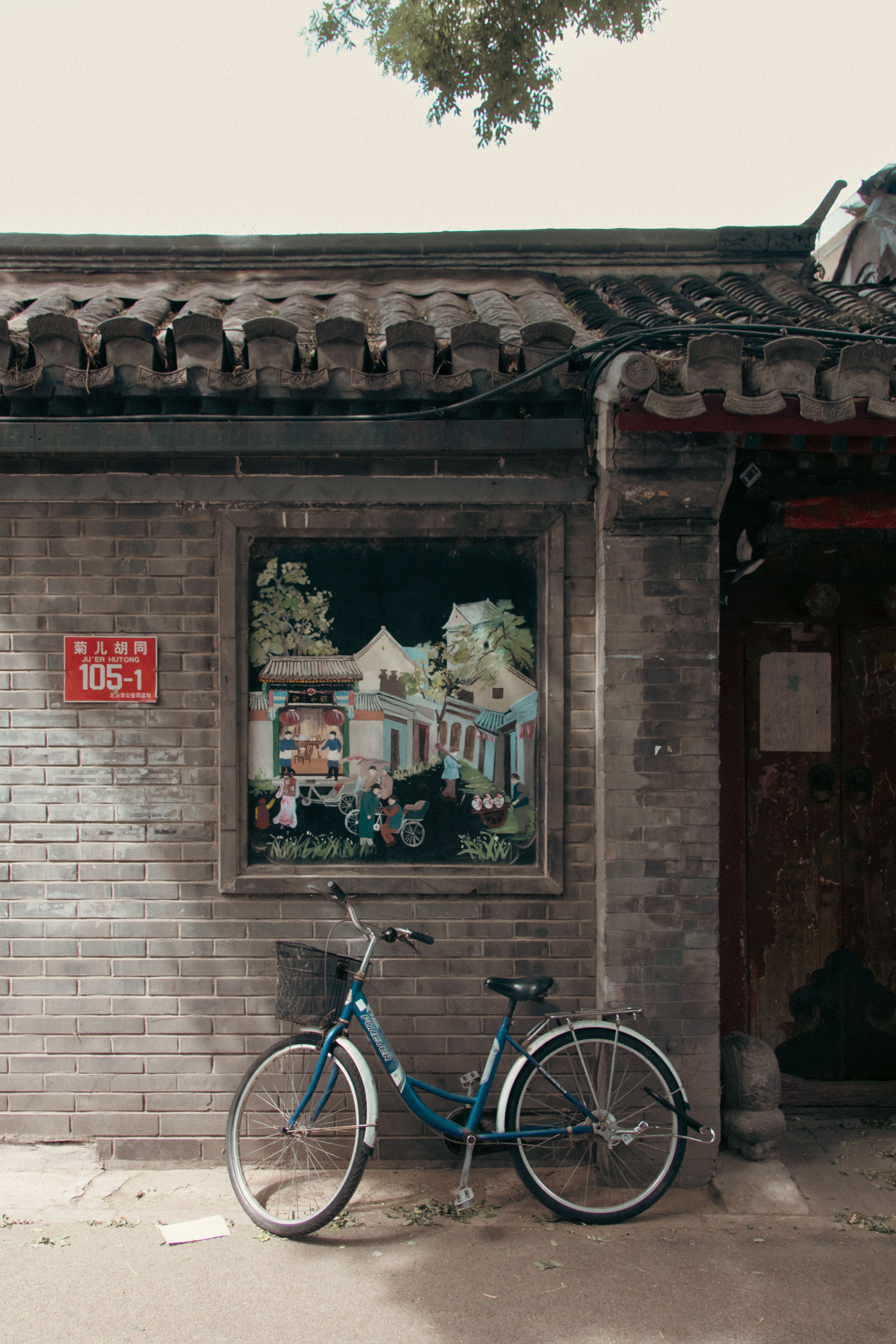 Fotomural Una bicicleta clásica azul apoyada contra una pared con pintura china tradicional en un entorno urbano.