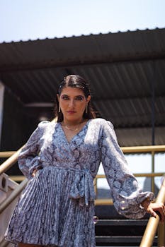 Stylish woman in patterned dress posing outdoors in sunlight.