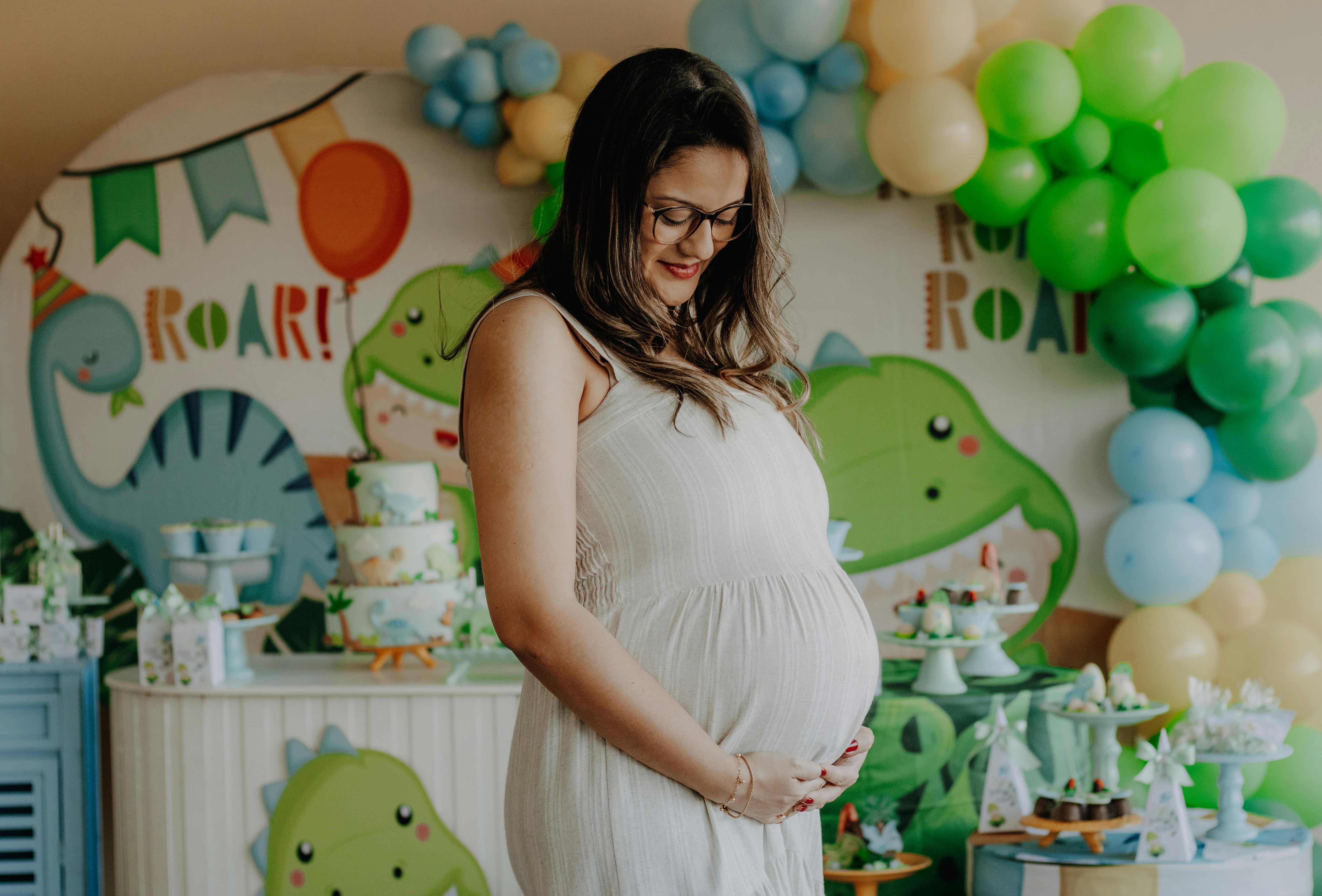 Smiling pregnant woman at a dinosaur-themed baby shower with colorful decorations.