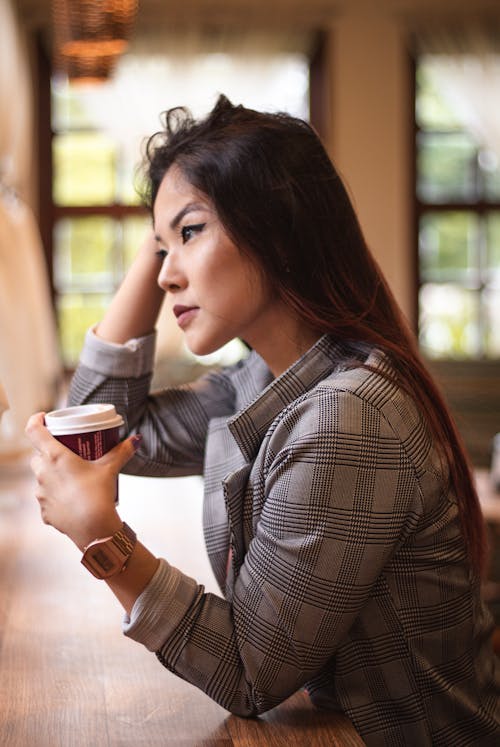 Free Selective Focus Side View Photo of Woman Sitting by Table Holding Plastic Cup Looking into the Distance Stock Photo