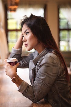 咖啡馆里，一位沉思的女人端着咖啡杯，看起来若有所思