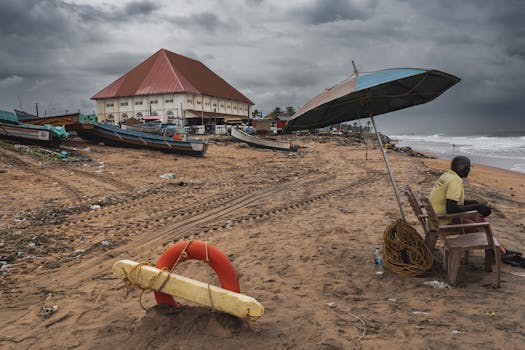 Stormy beach scene with boats, lifeguard, and large building under dark clouds, conveying a moody coastal atmosphere.