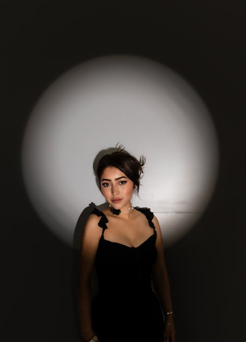 A woman in a black dress standing in front of a light