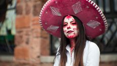 Woman in traditional Day of the Dead makeup and hat in Mexico City, vibrant cultural representation.