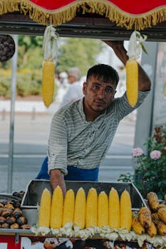Portrait of a street vendor with fresh corn display in an urban outdoor setting.