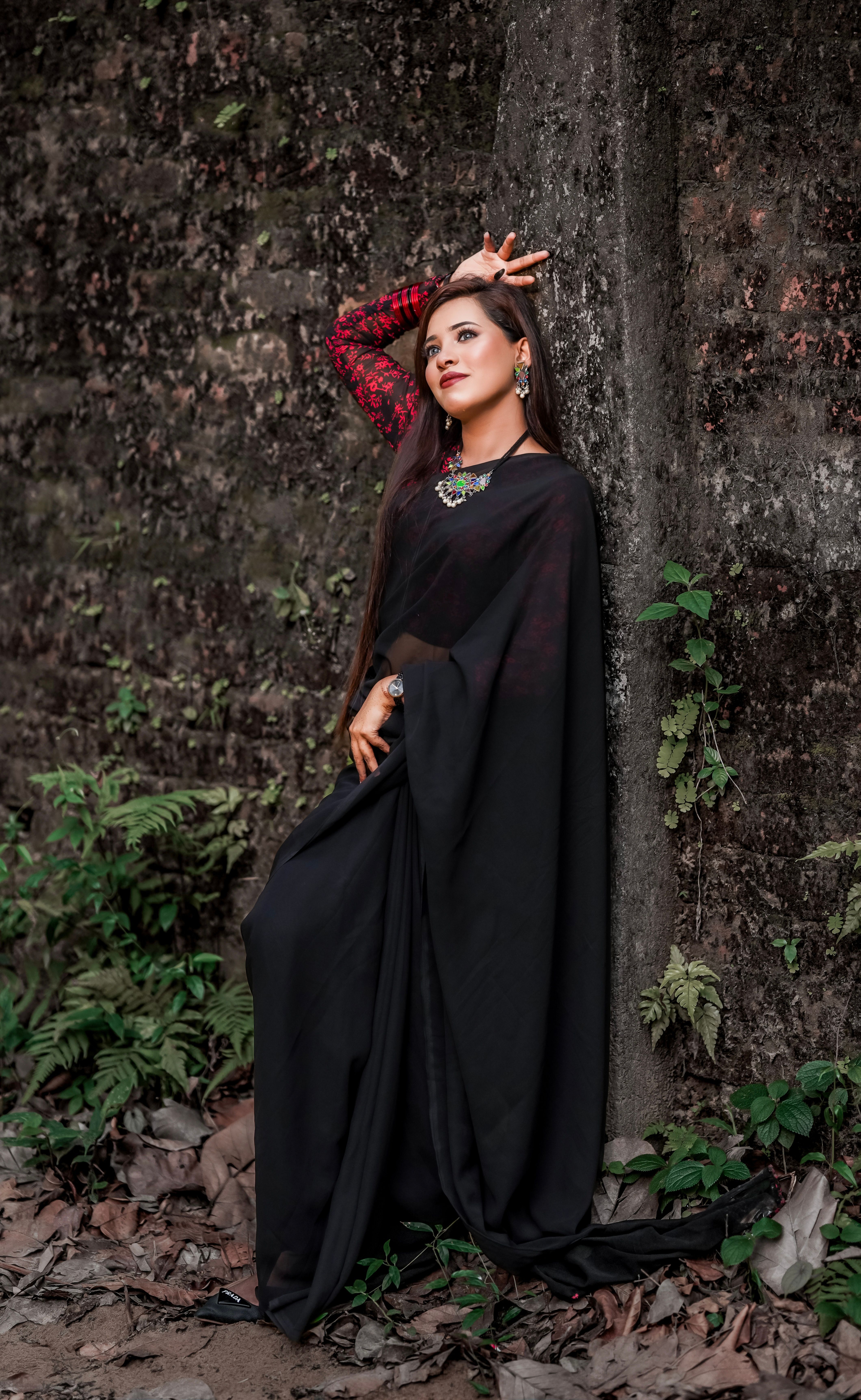 Young woman in black sari posing elegantly against a forest backdrop, showcasing traditional fashion.
