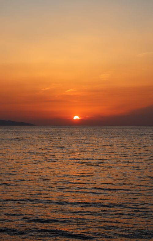 Free A breathtaking view of the sun setting over a tranquil ocean, casting a warm glow on the water's surface. Stock Photo