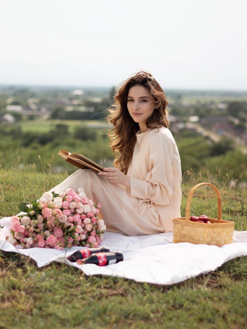 A woman sitting on a blanket with a book and flowers