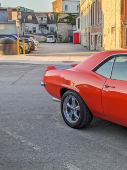 A classic red Chevrolet Camaro parked in a Kingston, Ontario city street at sunset.