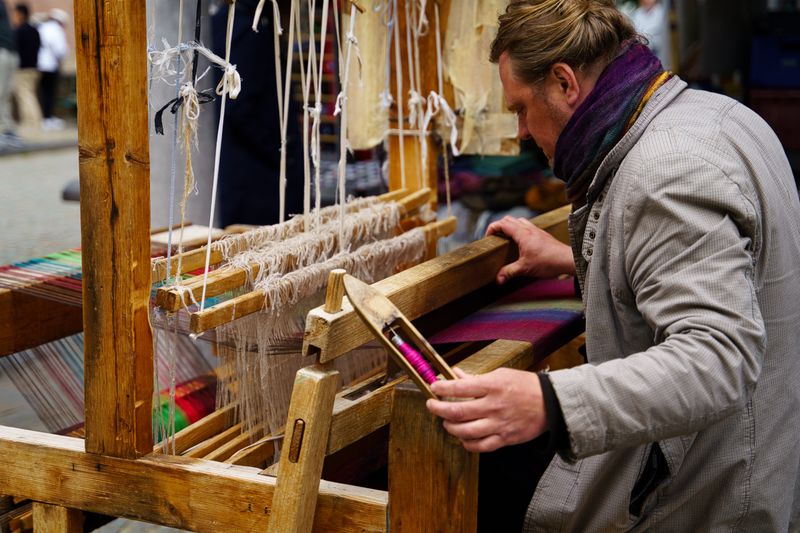 Skilled artisan weaving colorful fabric using a traditional wooden loom outdoors.