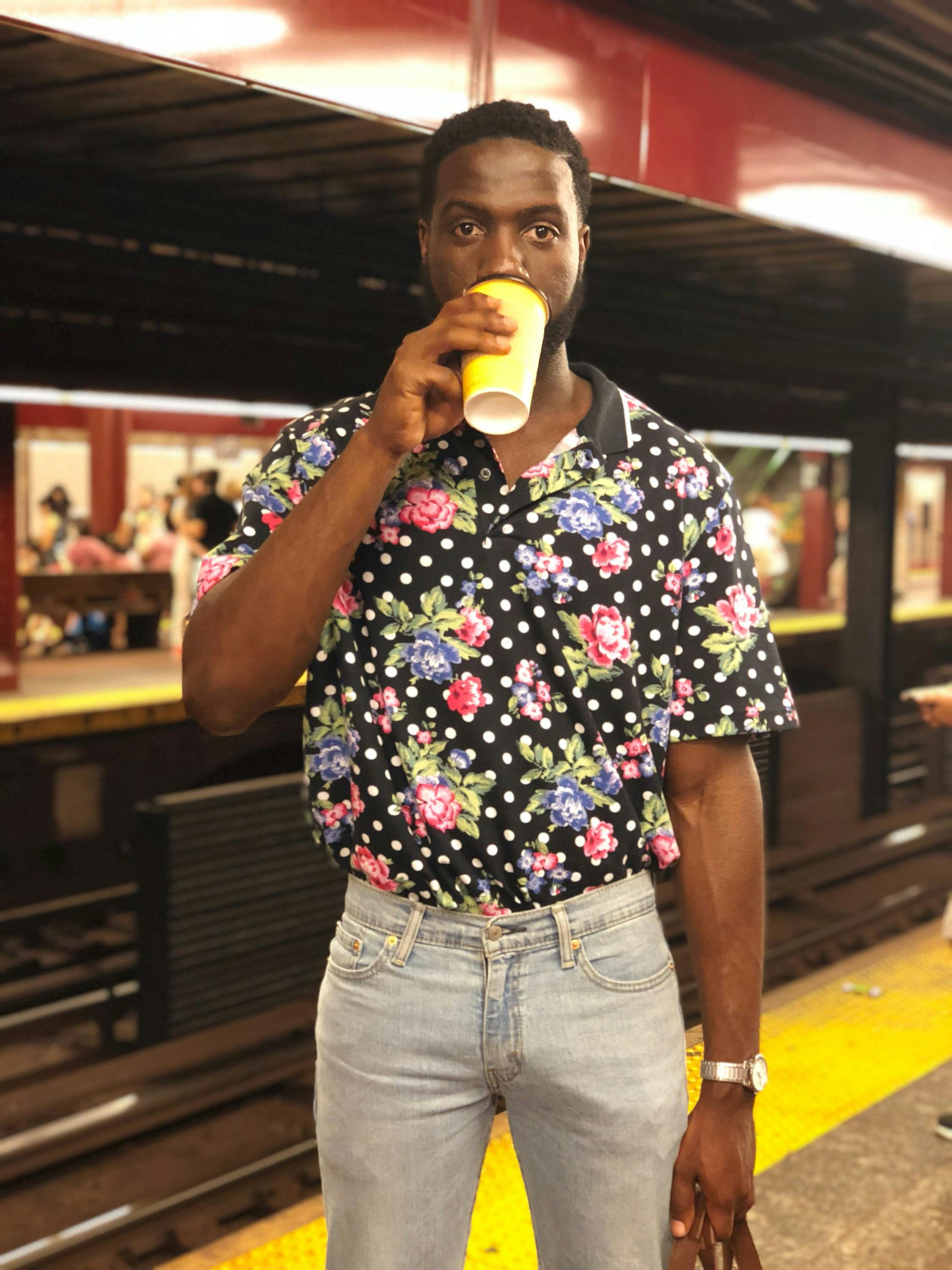 photo of man drinking from plastic cup posing while standing on subway platform