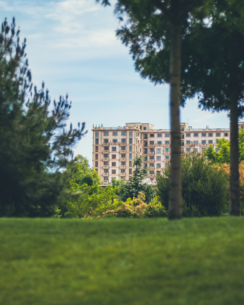 Free A tranquil park scene showcasing an apartment building framed by lush greenery and trees. Stock Photo