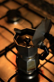 特写镜头中，不锈钢莫卡壶在室内炉子上煮着咖啡，营造出温暖迷人的氛围