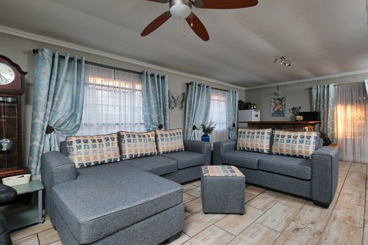 Stylish living room with blue sofas, elegant curtains, and a ceiling fan for a cozy feel.