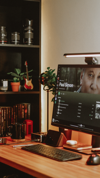 Warmly lit home office with computer, décor, and music on screen. Ideal for workspace inspirations.